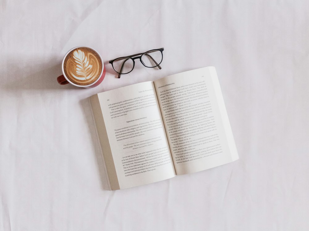 An open book beside a cup of coffee and reading glasses
